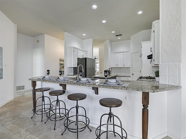 kitchen with stainless steel fridge with ice dispenser, white cabinetry, kitchen peninsula, a breakfast bar area, and tasteful backsplash