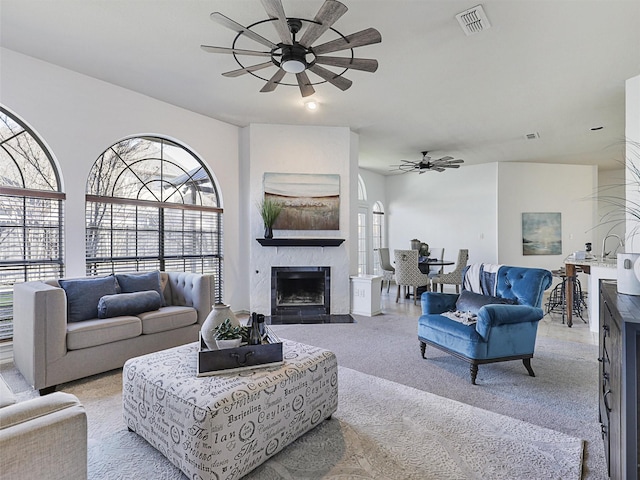 living area featuring light colored carpet, a fireplace with flush hearth, visible vents, and a ceiling fan