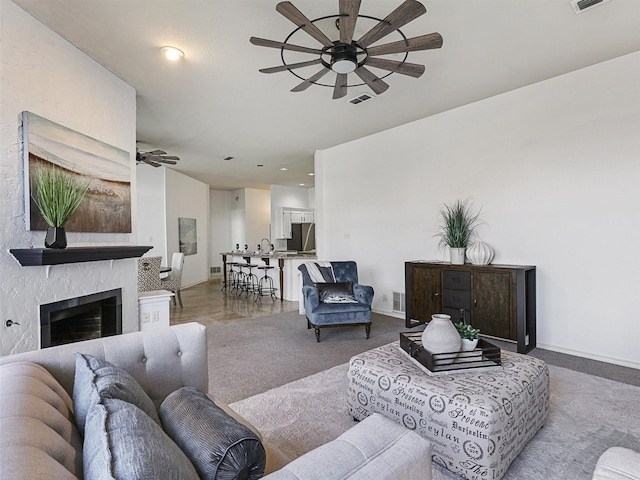 carpeted living room with ceiling fan, a fireplace, visible vents, and baseboards