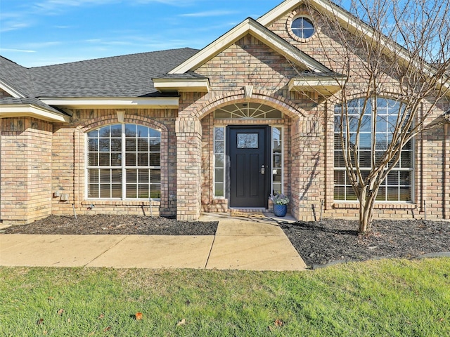view of exterior entry featuring brick siding and roof with shingles