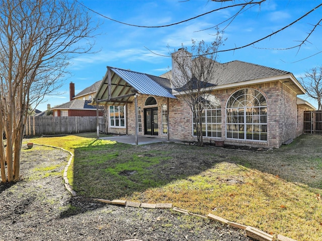 rear view of house featuring a patio, brick siding, a chimney, and a fenced backyard