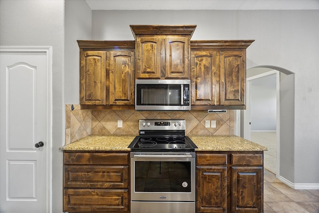 kitchen featuring light tile patterned floors, decorative backsplash, light stone counters, and stainless steel appliances