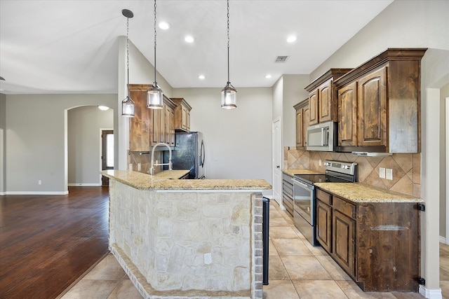 kitchen featuring appliances with stainless steel finishes, decorative backsplash, hanging light fixtures, and light stone countertops