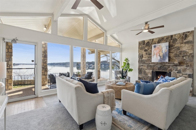 living room with ceiling fan, a water view, a fireplace, and lofted ceiling with beams