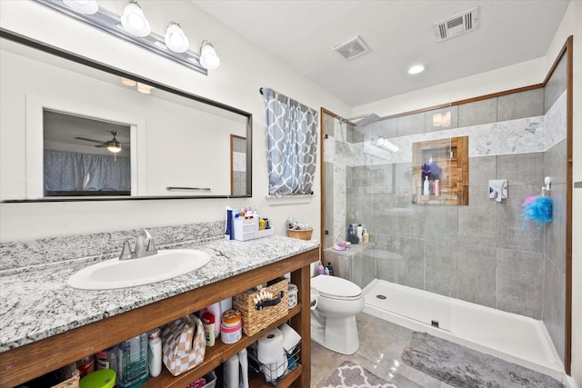 bathroom featuring toilet, ceiling fan, tiled shower, tile patterned flooring, and vanity