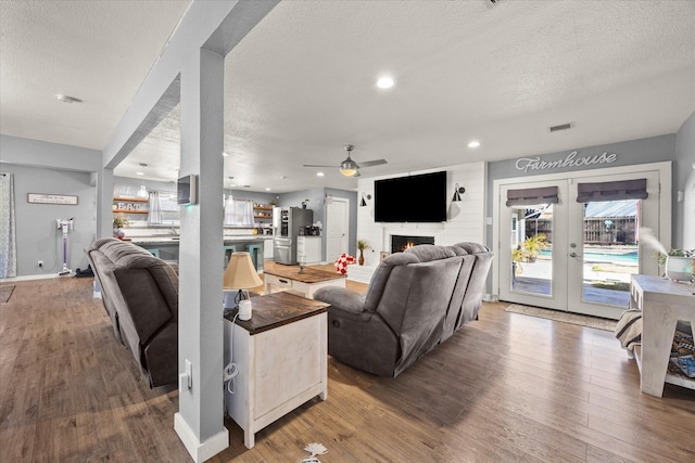 living room featuring hardwood / wood-style floors, ceiling fan, a large fireplace, french doors, and a textured ceiling