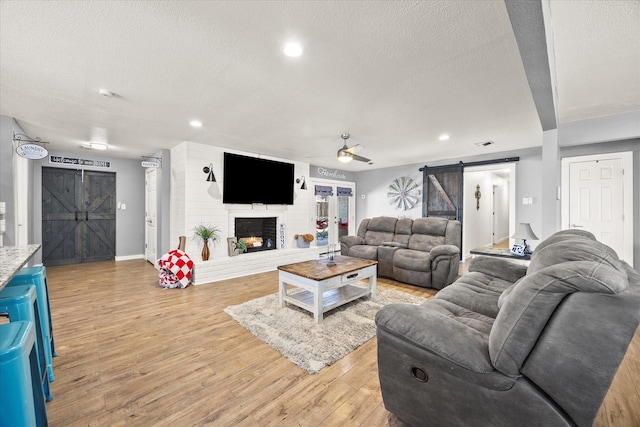 living room with a textured ceiling, a fireplace, a barn door, and light hardwood / wood-style flooring