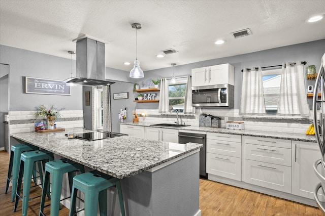 kitchen featuring pendant lighting, white cabinets, appliances with stainless steel finishes, island exhaust hood, and sink