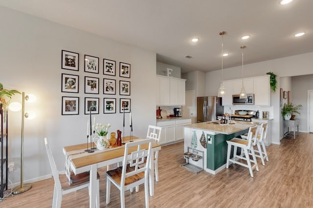 kitchen with stainless steel appliances, an island with sink, white cabinetry, and decorative light fixtures