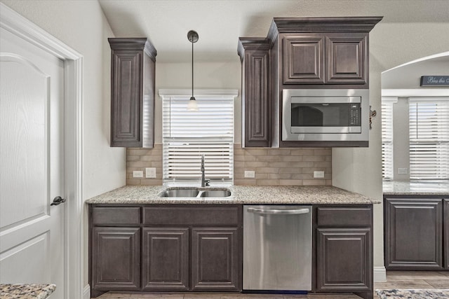 kitchen with appliances with stainless steel finishes, tasteful backsplash, hanging light fixtures, light stone counters, and sink