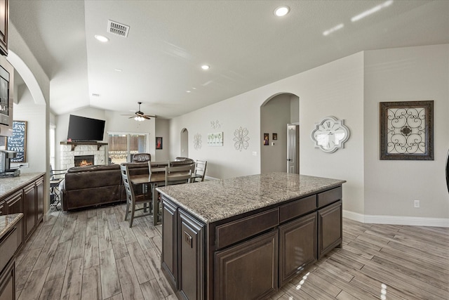 kitchen with ceiling fan, a kitchen island, light hardwood / wood-style flooring, and a stone fireplace