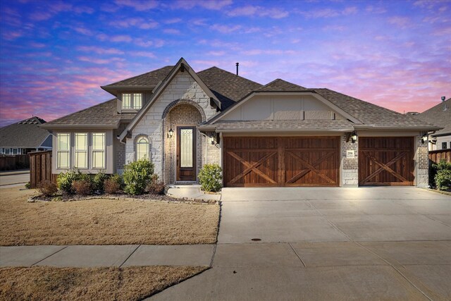 view of front of house with concrete driveway, a garage, stone siding, and a shingled roof
