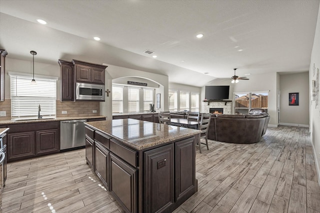 kitchen featuring a stone fireplace, stainless steel appliances, decorative light fixtures, lofted ceiling, and a center island