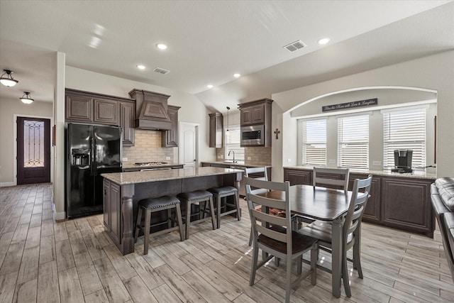 kitchen featuring backsplash, a kitchen island, custom exhaust hood, appliances with stainless steel finishes, and light stone counters