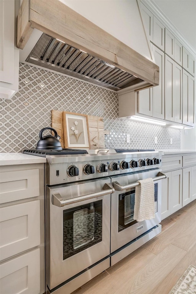 kitchen featuring double oven range, custom exhaust hood, light hardwood / wood-style flooring, backsplash, and white cabinets