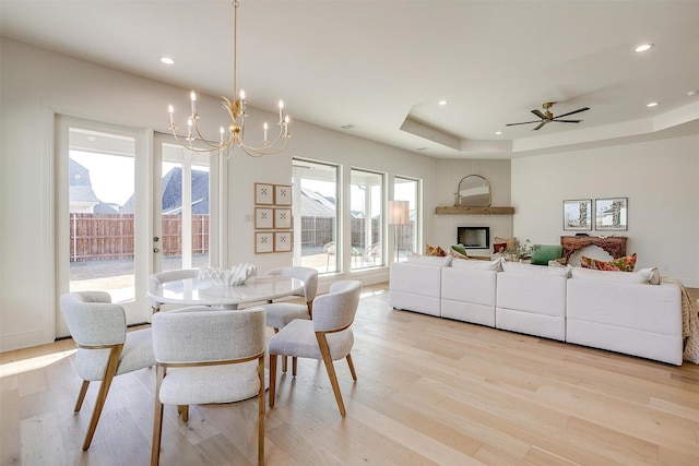 dining room featuring a raised ceiling, a fireplace, ceiling fan with notable chandelier, and light hardwood / wood-style floors