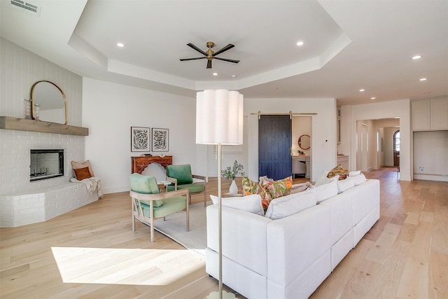 living room featuring ceiling fan, a barn door, a tray ceiling, and light hardwood / wood-style flooring