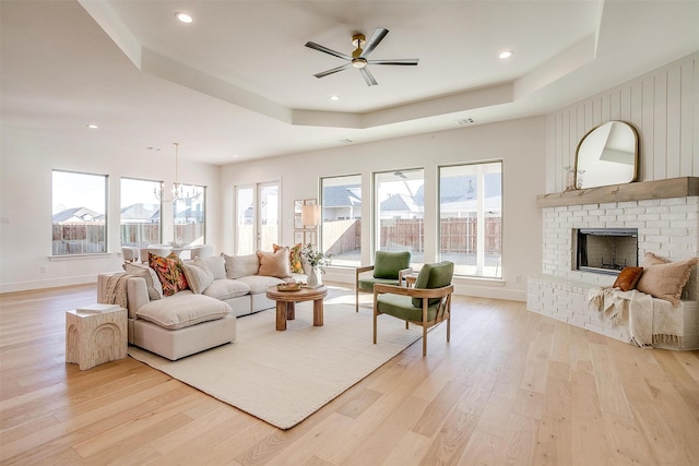 living room with light wood-type flooring, a raised ceiling, and a fireplace