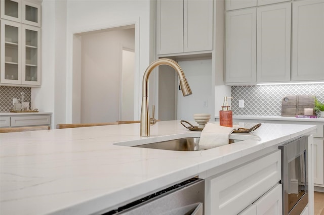 kitchen featuring light stone countertops, white cabinetry, backsplash, and sink