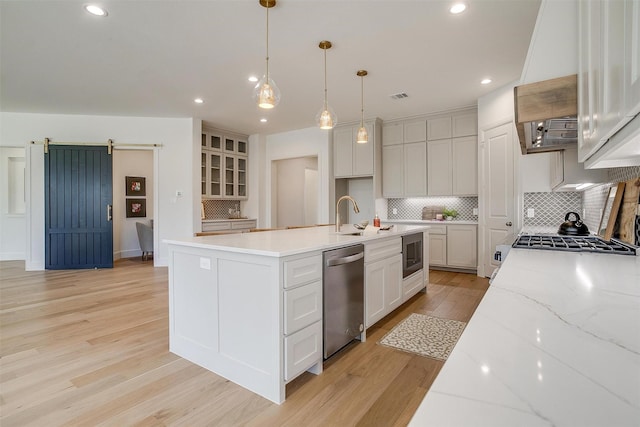 kitchen with pendant lighting, dishwasher, white cabinetry, a barn door, and built in microwave