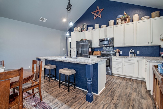 kitchen with white cabinetry, an island with sink, stainless steel appliances, decorative light fixtures, and a breakfast bar