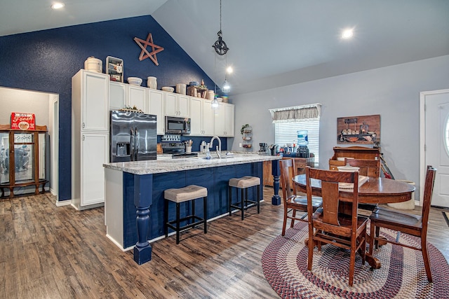 kitchen with appliances with stainless steel finishes, white cabinetry, dark hardwood / wood-style floors, a center island with sink, and decorative light fixtures