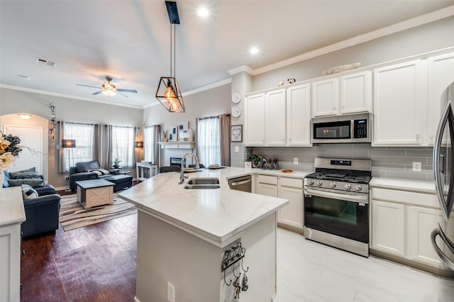 kitchen featuring decorative light fixtures, appliances with stainless steel finishes, open floor plan, white cabinetry, and a sink