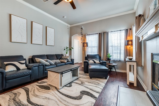 living room with baseboards, arched walkways, ornamental molding, dark wood-type flooring, and a fireplace