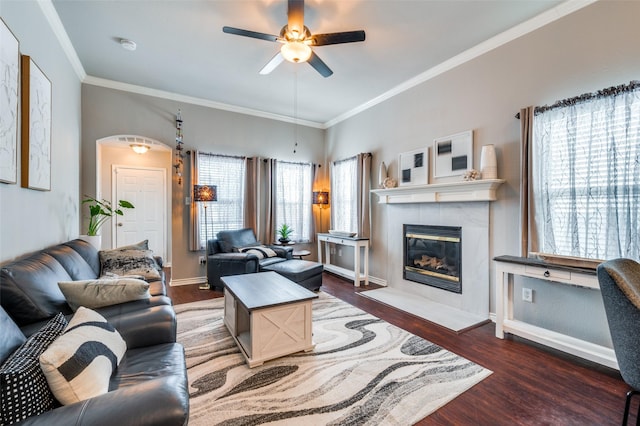 living room with arched walkways, a tile fireplace, dark wood-type flooring, baseboards, and ornamental molding