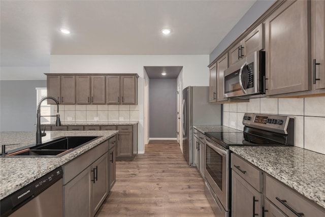 kitchen with light stone counters, light wood finished floors, a sink, decorative backsplash, and stainless steel appliances