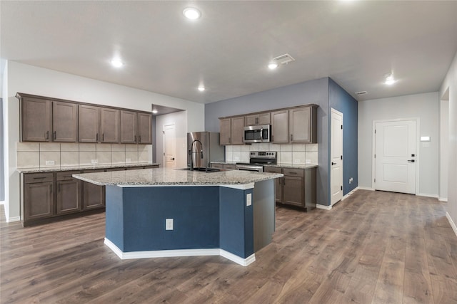 kitchen featuring dark wood finished floors, a center island with sink, stainless steel appliances, and a sink