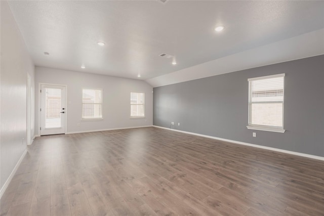 unfurnished room with a wealth of natural light, visible vents, wood finished floors, and vaulted ceiling