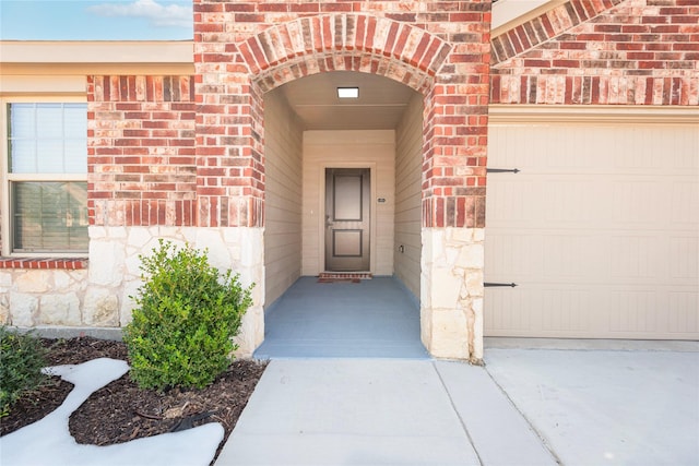 doorway to property featuring stone siding, brick siding, and an attached garage