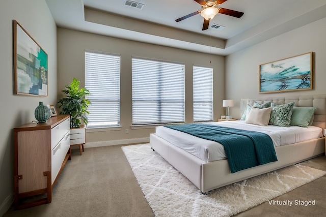 carpeted bedroom with ceiling fan, multiple windows, and a tray ceiling