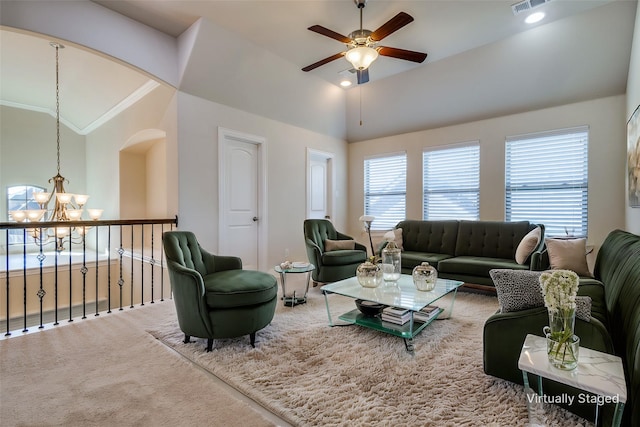 living room with ceiling fan with notable chandelier, ornamental molding, carpet floors, and high vaulted ceiling