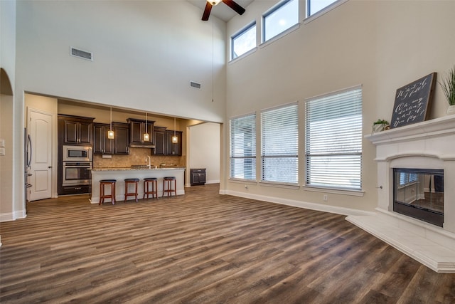 living room with ceiling fan, plenty of natural light, dark hardwood / wood-style flooring, and a towering ceiling