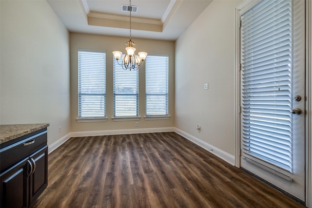 unfurnished dining area with dark hardwood / wood-style floors, a chandelier, a healthy amount of sunlight, and a raised ceiling