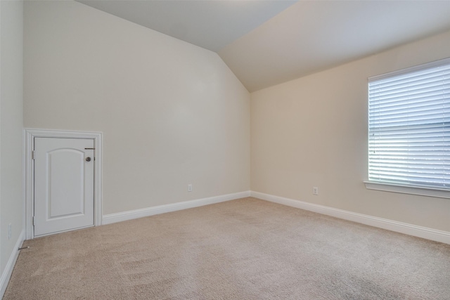 unfurnished room with a healthy amount of sunlight, lofted ceiling, and light colored carpet