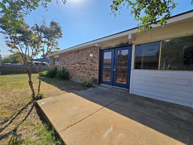 view of exterior entry with french doors, a lawn, and a patio