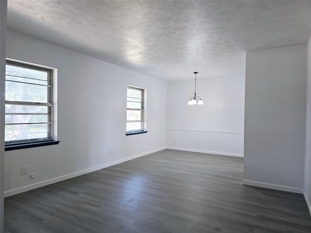 empty room featuring a textured ceiling, a healthy amount of sunlight, dark hardwood / wood-style floors, and a notable chandelier