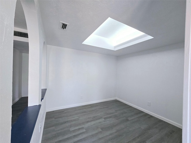 unfurnished room featuring a skylight, dark hardwood / wood-style floors, and a textured ceiling