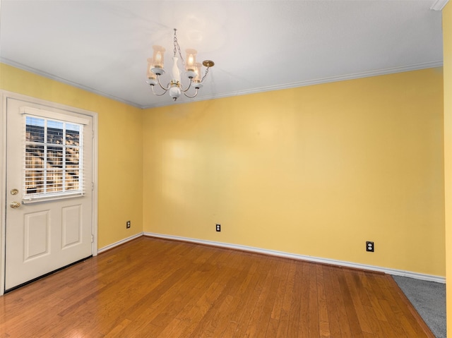 empty room with hardwood / wood-style flooring, ornamental molding, and an inviting chandelier