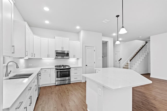 kitchen featuring appliances with stainless steel finishes, a kitchen island, decorative light fixtures, white cabinetry, and sink