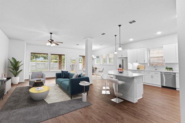 living room featuring ceiling fan, sink, hardwood / wood-style floors, and decorative columns