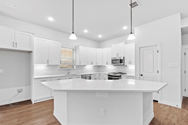 kitchen featuring hanging light fixtures, a kitchen island, stainless steel appliances, and white cabinetry