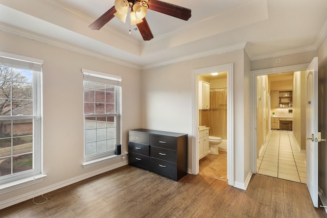 bedroom with ceiling fan, a tray ceiling, dark hardwood / wood-style flooring, and ensuite bath