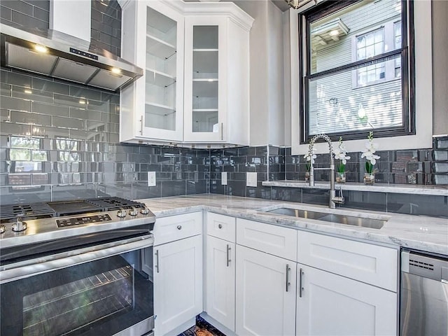 kitchen with appliances with stainless steel finishes, sink, white cabinets, and wall chimney range hood