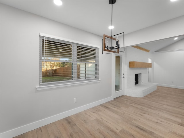 unfurnished living room with a brick fireplace, lofted ceiling, and light hardwood / wood-style flooring