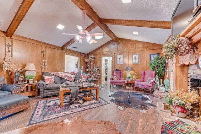 living room with light hardwood / wood-style flooring, ceiling fan, vaulted ceiling with beams, wooden walls, and a textured ceiling