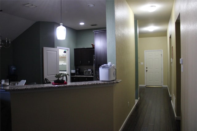 kitchen with dark wood-type flooring, decorative light fixtures, kitchen peninsula, and dark stone countertops